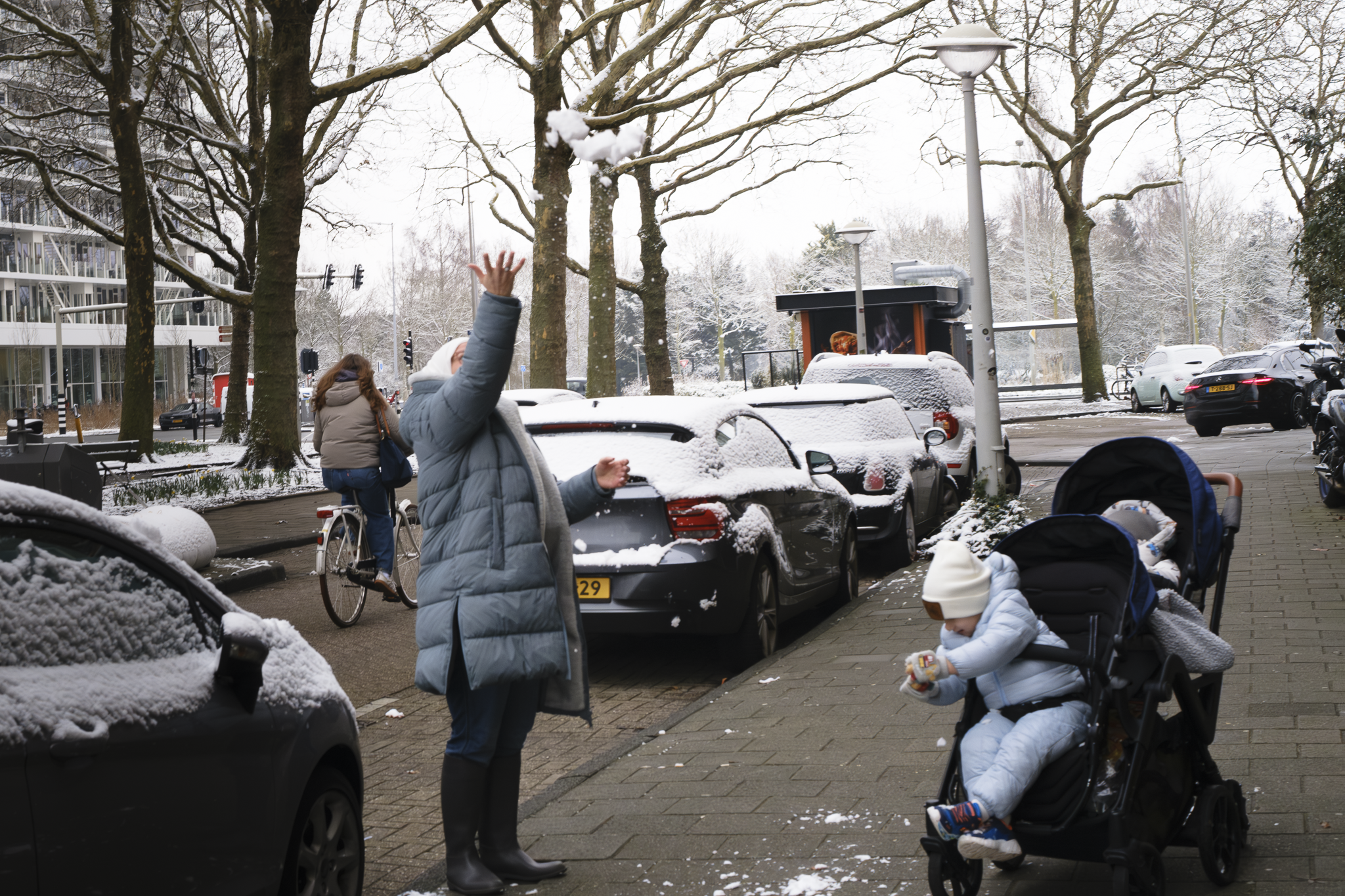A woman throwing some snow up, while kids in a stroller play with snow. Amsterdam 2026